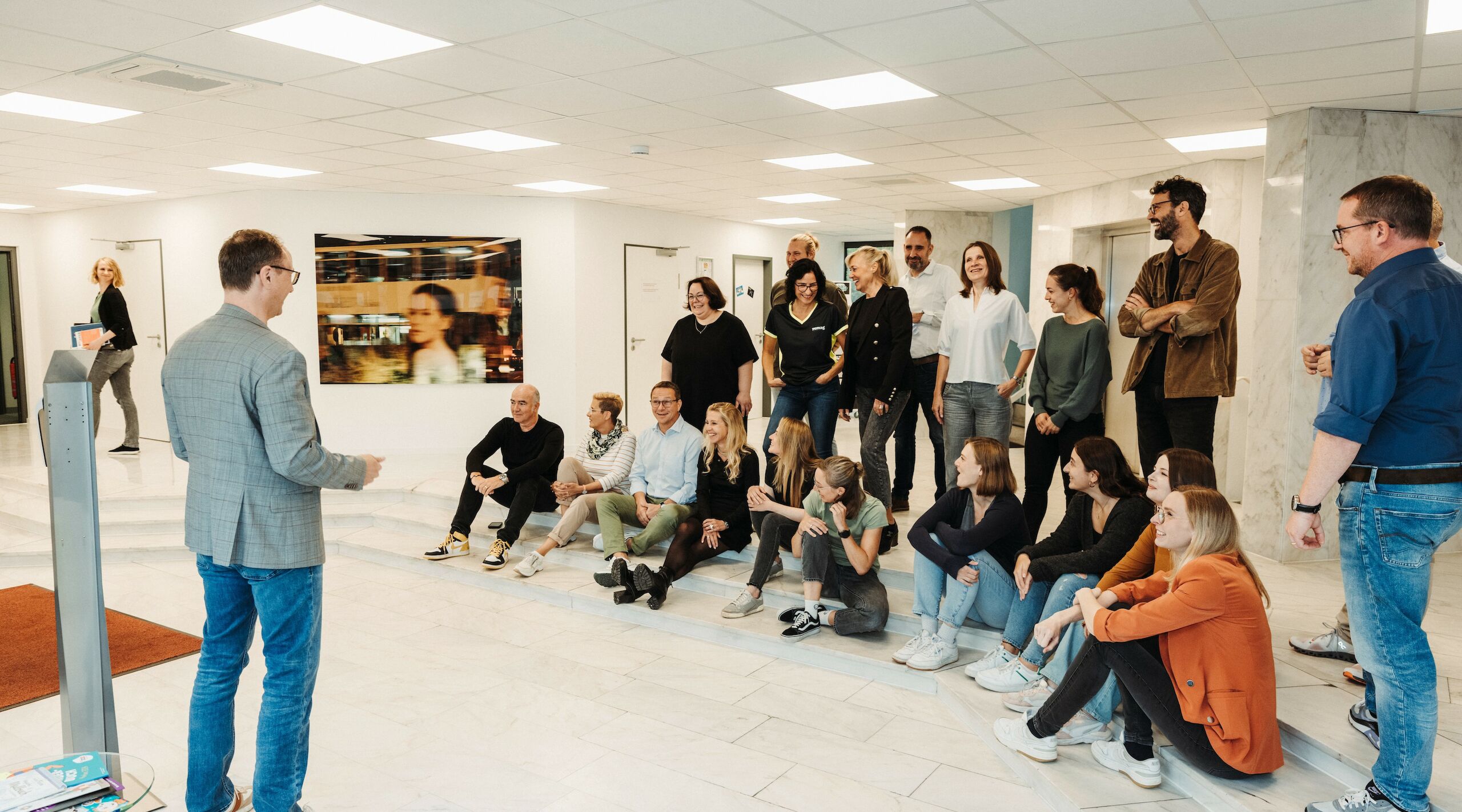 Eine Mitarbeiterversammlung im Foyer mit einem Mann, der vor der Gruppe steht und spricht