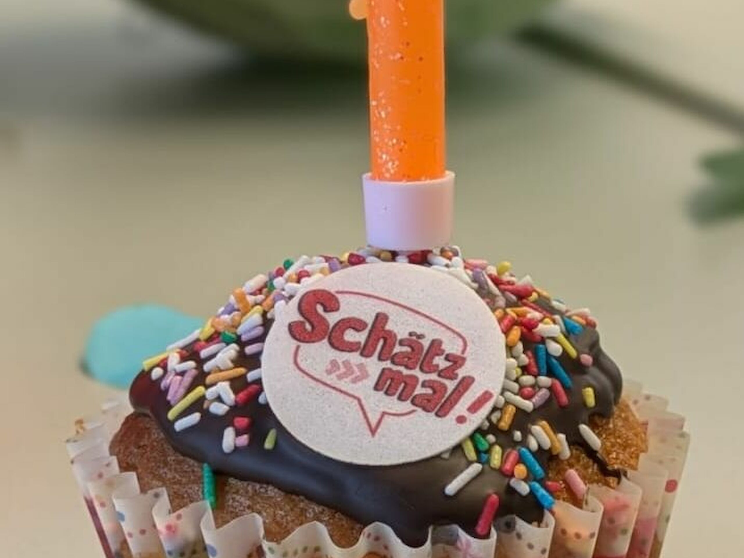 Foto eines Muffins mit Schätz mal! Logo und einer Kerze